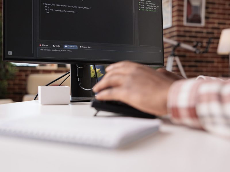 Selective focus on computer screen of african american programmer working remote from home developing software on pc. System developer writing code on personal computer typing algorithm on keyboard.